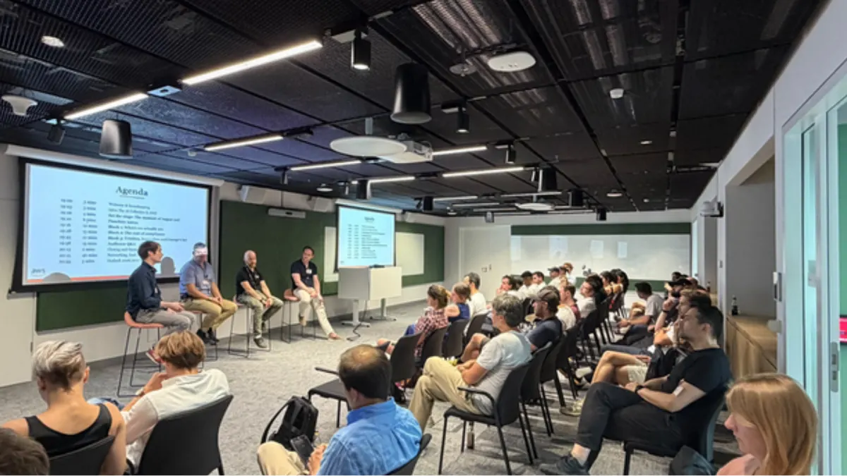 Panel of four speakers on stools in front of an audience of about forty people