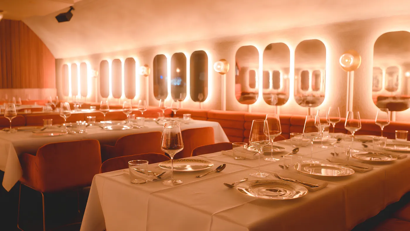 Papillon dining room set for dinner, long white tables in front of lit oval mirrors